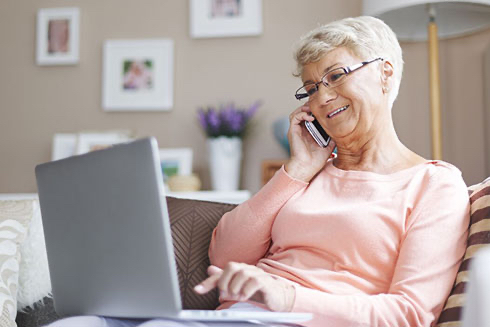 A senior woman talking on her cell phone while using a laptop.