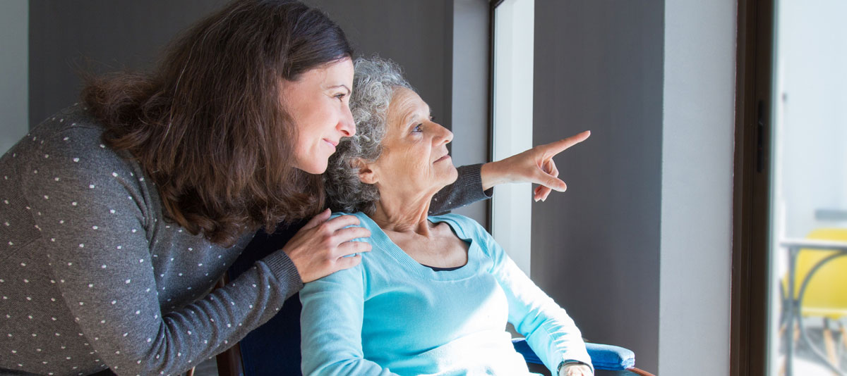 Mother and daughter looking out window of senior living apartment