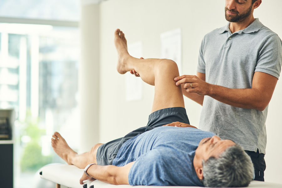 A senior man stretches with a physical therapist.