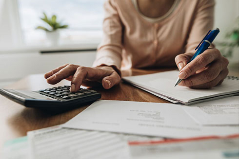 Close up of a senior woman's hands working with a calculator and writing notes down.