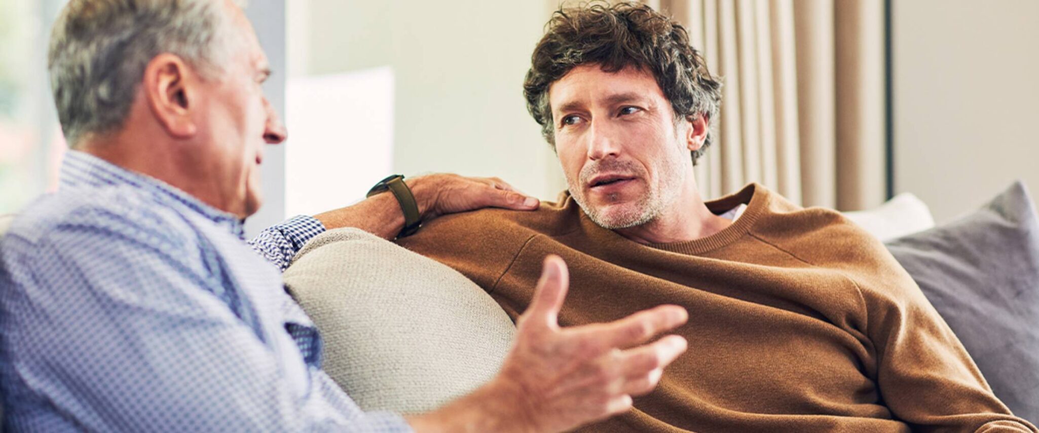 son and his elderly father have a discussion on the couch