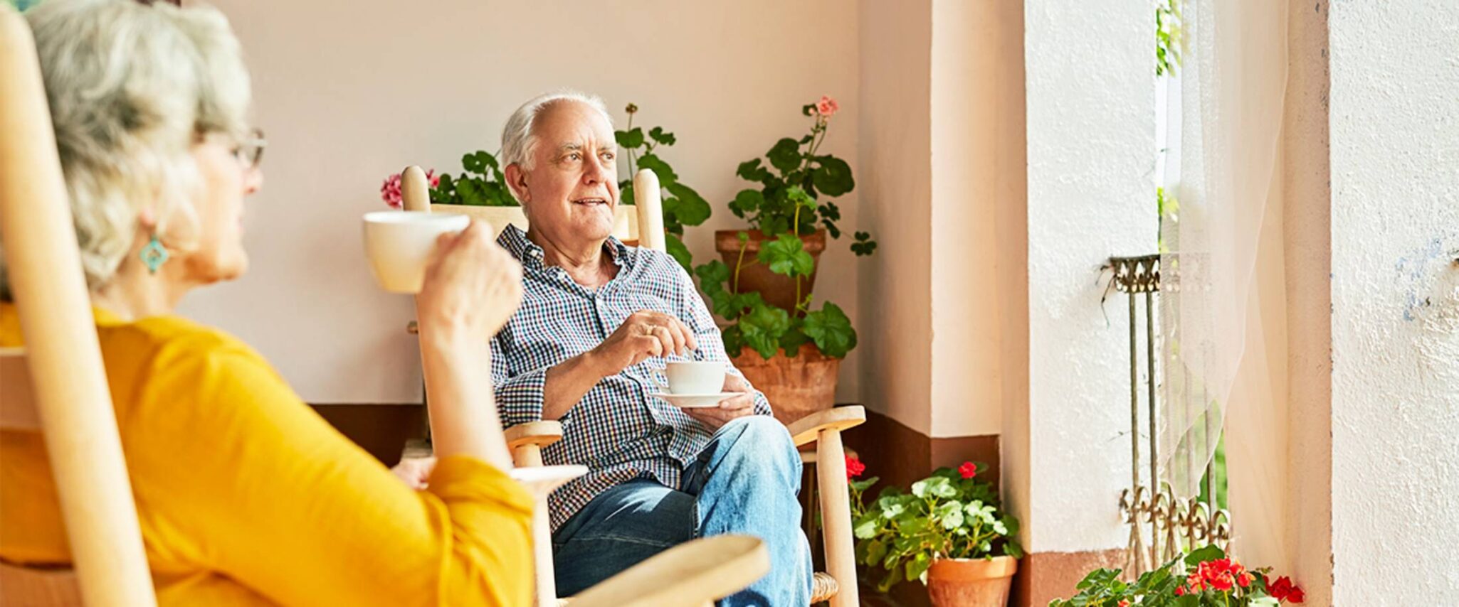 A senior man and senior woman sit in rocking chairs enjoying the sunny windows