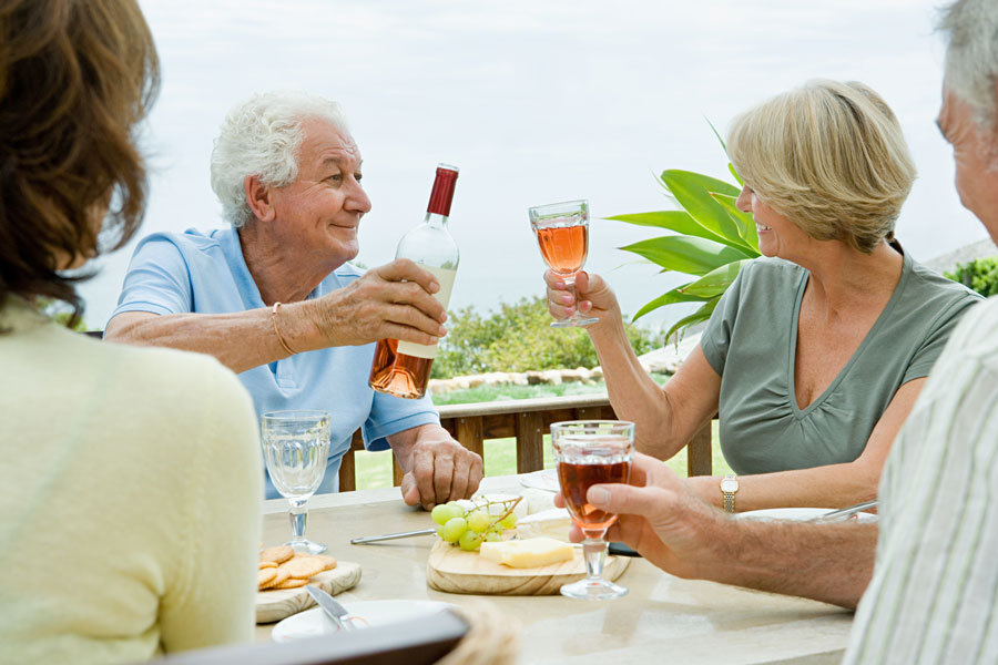 A group of seniors share a bottle of wine with a charcuterie board out on a patio.