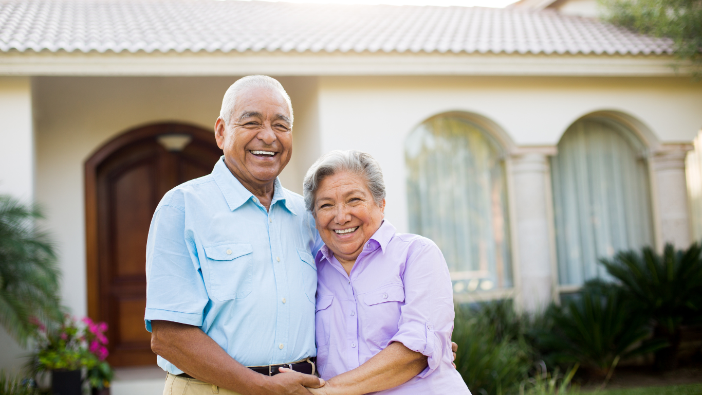 A woman and a man embrace in front of a home