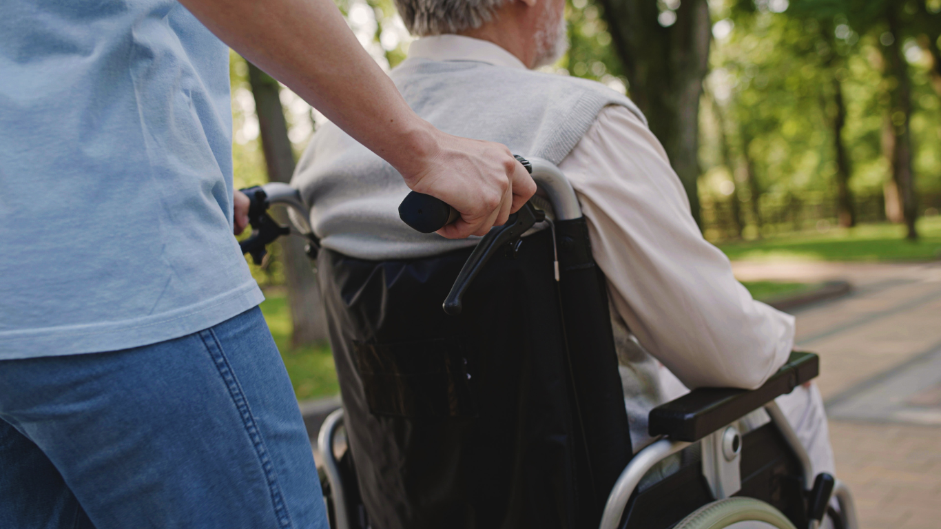 Blog Images – 2025-07-23T095946.163 Back shot of senior man being pushed in a wheelchair by his caretaker