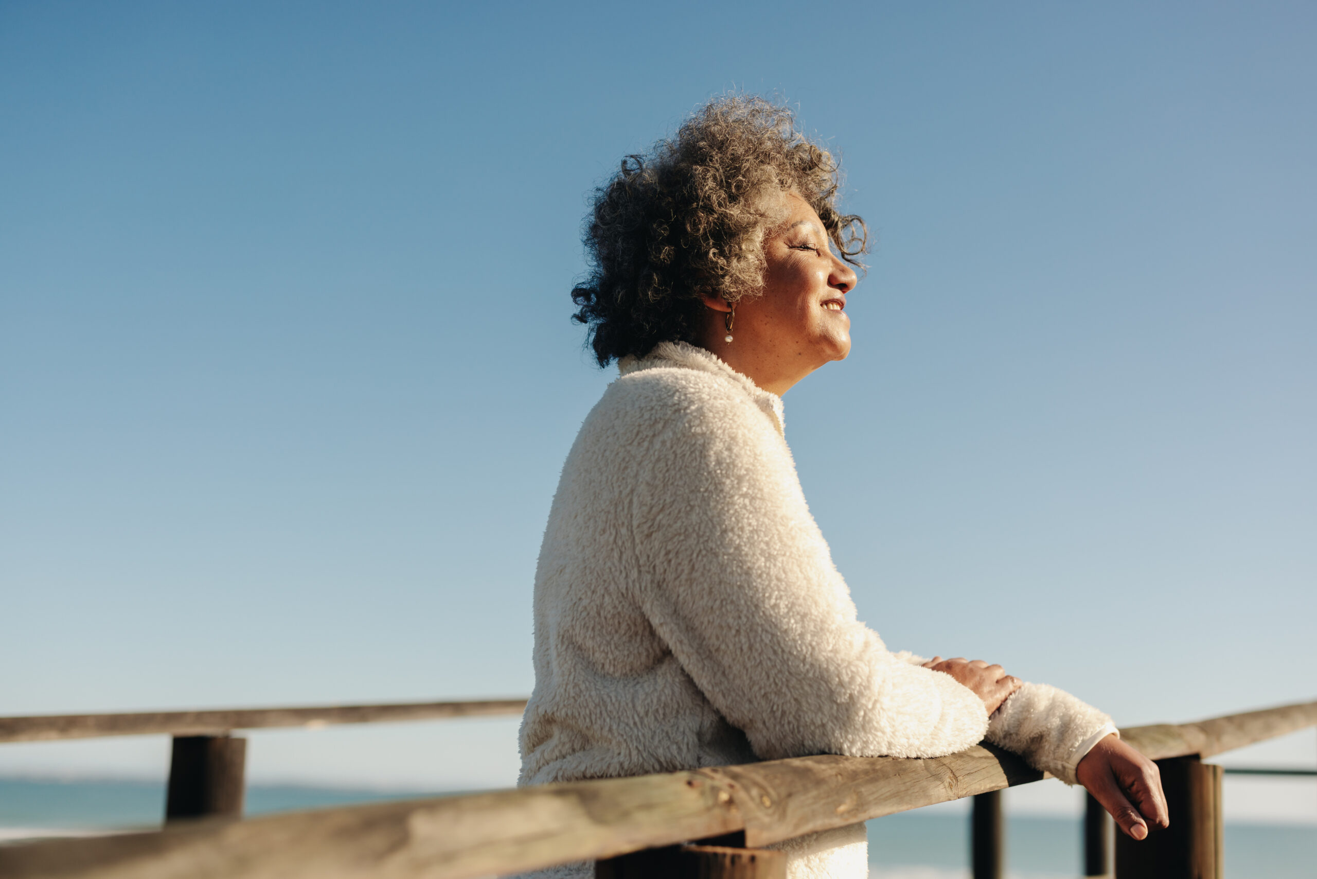 A woman leans against a wood beach boardwalk and soaks up the sun