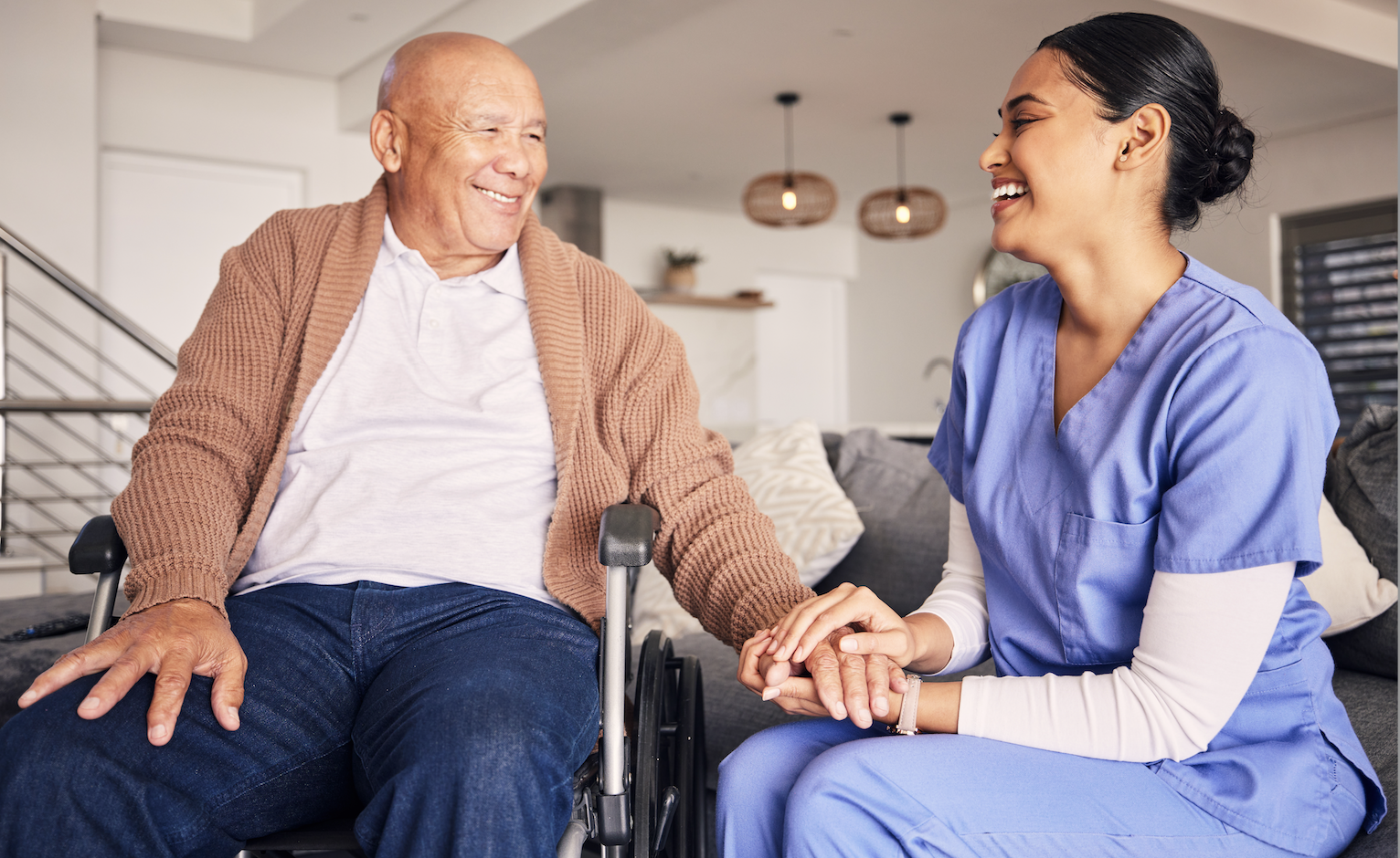 Smiling senior man in wheelchair holding the hands of a female nurse