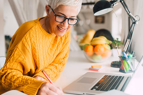 A senior woman works at a desk station on a laptop.