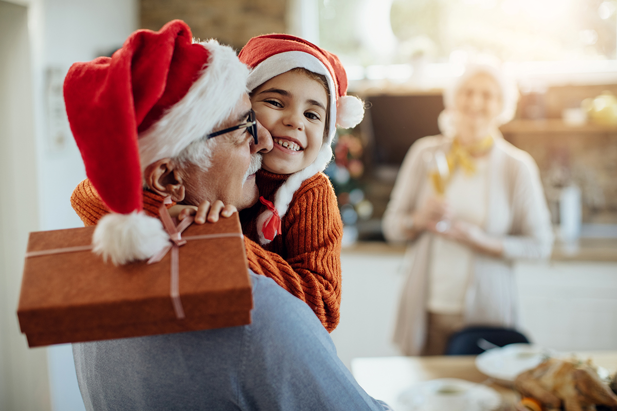 Joyful granddaughter and grandfather embracing after exchanging gifts on Christmas day at home.